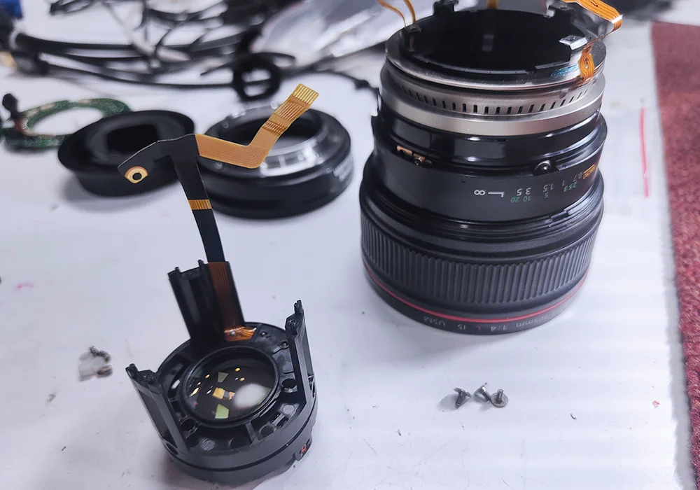 Photographie d'un objectif d'appareil photo démonté pour mieux le réparer.